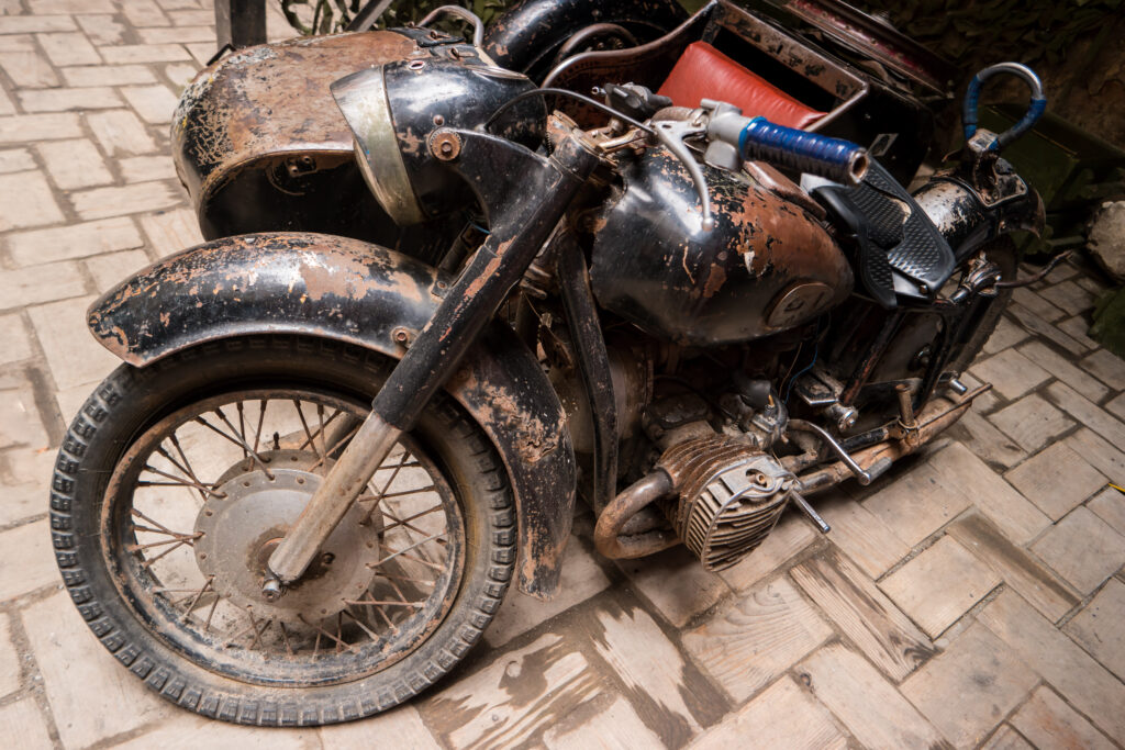 A close-up of a black, heavily rusted and old motorcycle with a sidecar, symbolizing bike scrapping and the recycling process for end-of-life vehicles in Bengaluru.