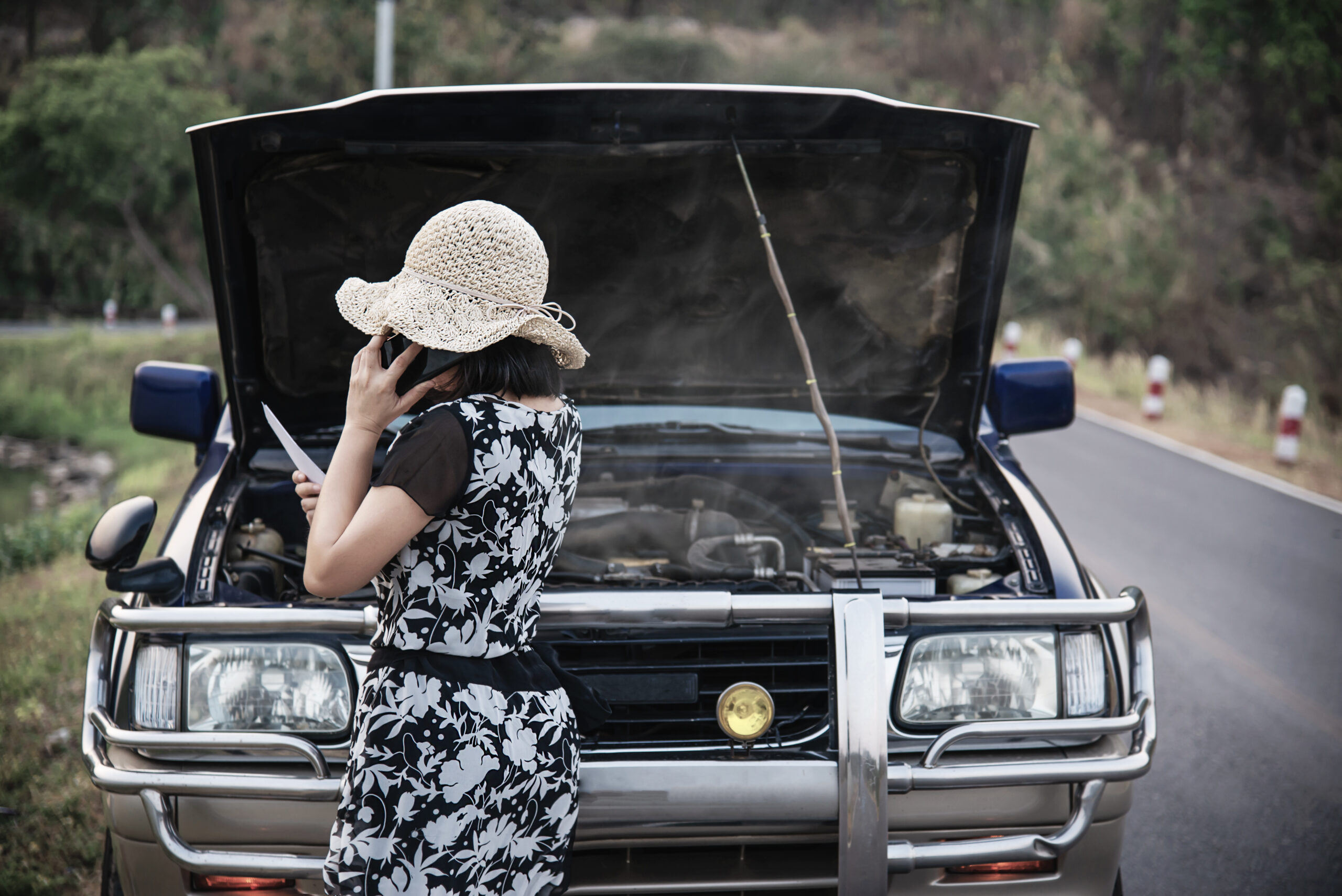 Asian woman calling repairman or insurance staff to fix a car engine problem on a local road - people with car problem transportation concept