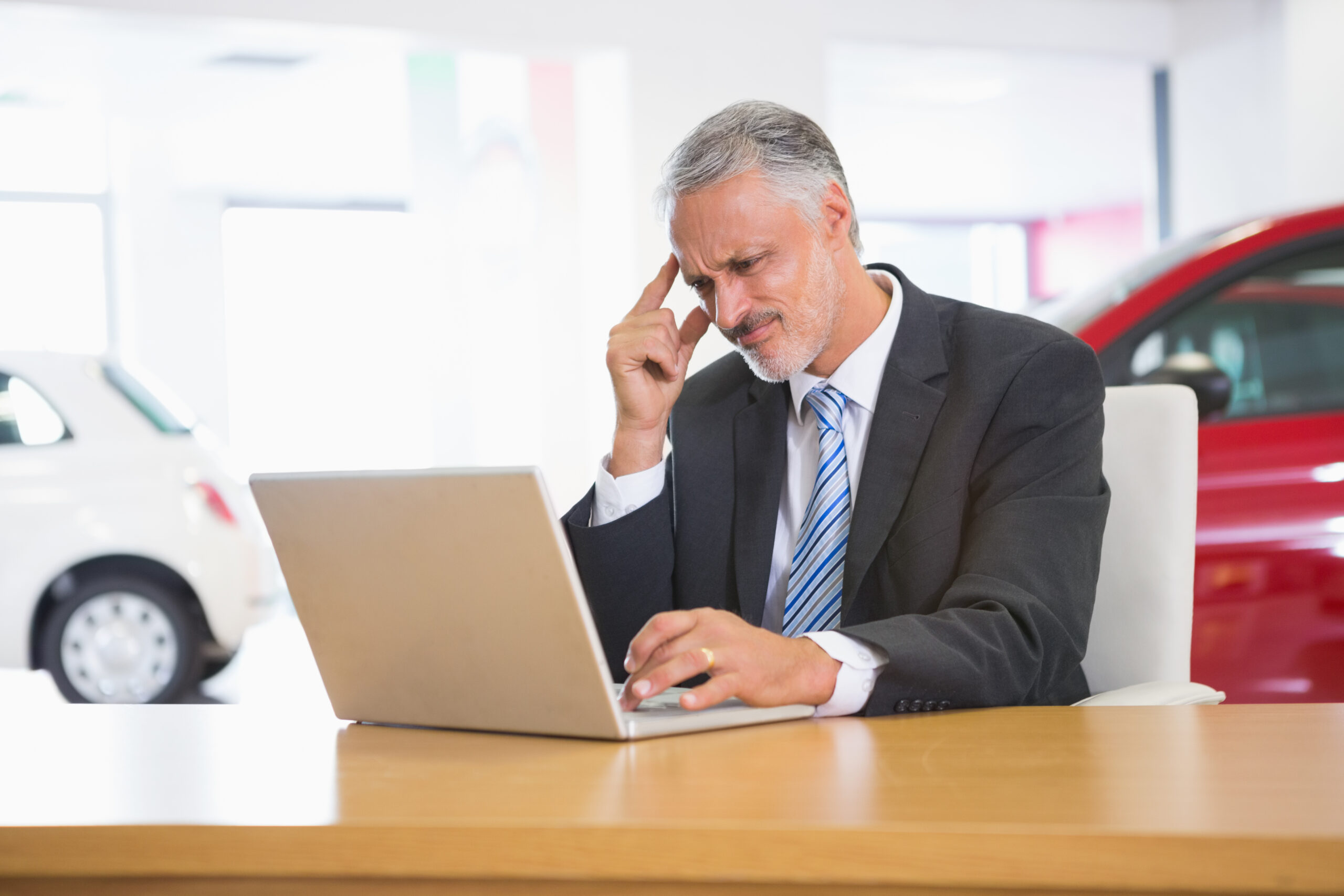 Upset businessman working on computer at new car showroom